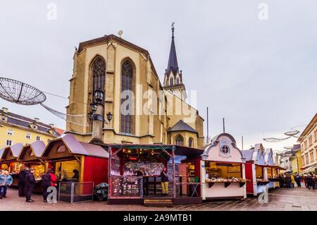 Villach, Österreich (16 November 2019) - Die Kirche von St. Jakob durch die hölzerne kleine Boutiquen der Weihnachtsmarkt umgeben Stockfoto