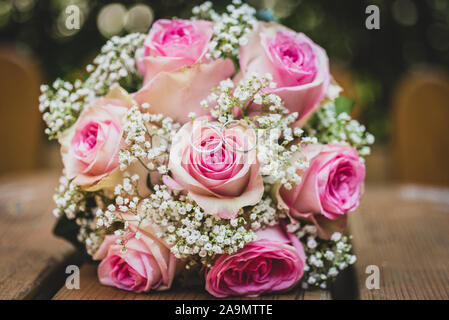 Wedding Bouquet mit rosa Rosen auf Holztisch mit Ringen. Hochzeit Ringe und schöne Hochzeit Strauß auf natürliche Holz Schreibtisch mit Natur in backgrou Stockfoto