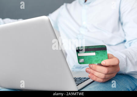 Online Shopping. Junger Mann studio Sitzen auf einem Sofa auf grau, Online Shopping auf Laptop Zahlung per EC-Karte für den Kauf der isoliert-up Stockfoto