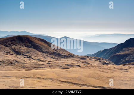 Blick von oben auf einen Panoramablick auf die Berge Landschaft bei аutumn, abwechselnd Gebirge, im Nebel und dem klaren, blauen Himmel im Hintergrund abgedeckt. Stockfoto