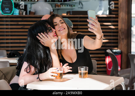 Zwei junge Frauen sind mit ihrem Smartphone in eine Terrasse von einem Pub. Lifestyle, Technik Stockfoto