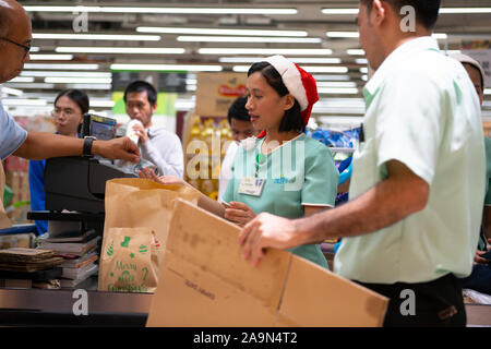 Ein Mann zahlt für Reihen Hände Geld auf ein Mitglied des Personals weihnachten Hüte tragen, während sie an der Kasse in einem Supermarkt, Cebu City, Philippin Stockfoto