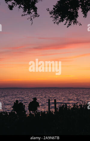 Die Silhouette eines Paar sitzt auf einem Dock beobachten die rosa Sonnenuntergang über See Apopka in Florida. Stockfoto