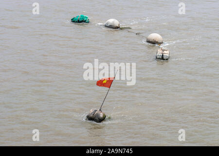 Lange Tau Fluss, Vietnam - 12. März 2019: Provisorische Bojen auf braunen Wasser, einer mit vietnamesischen Nationalen falg von Gelber Stern auf Rot. Stockfoto