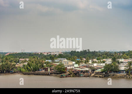 Lange Tau Fluss, Vietnam - 12. März 2019: Riverside Phuoc Khanh Dorf mit mehreren Häusern. Hellblau cloudscape und grüne Vegetation entlang der Ufer. Stockfoto