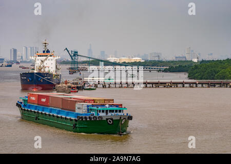 Lange Tau Fluss, Vietnam - März 12, 2019: Fluss container Boot segelt auf braunem Wasser vor phuoc Khanh Petroleum Pier, wo Prime Sands ist Stockfoto