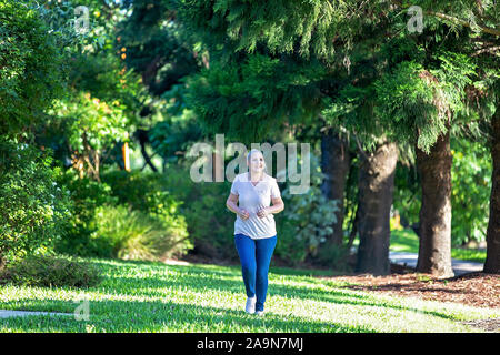 Frau joggen in botanischen Gärten mit späten Nachmittag Licht, das durch die Bäume Stockfoto