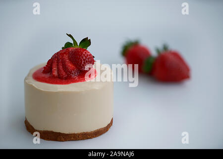 Nahaufnahme einer hausgemachten Käsekuchen mit Erdbeersauce und frische Erdbeeren unscharf im Hintergrund Stockfoto