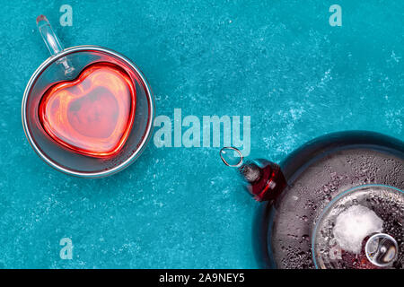 Blick von oben auf die roten Hibiskus Tee Teekanne aus Glas und Herzförmige Schale auf blauen Tabelle Stockfoto