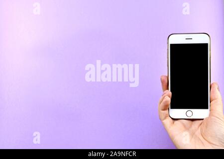Smartphone mit einem schwarzen Bildschirm in der Hand gedreht, auf einem violetten Hintergrund. Stockfoto