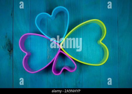 Farbige herzförmige Ausstechform Zahlen bilden eine dekorative Blüte, sitzen auf den blauen Hintergrund und Holz gesehen von oben Stockfoto