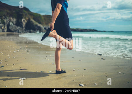 Eine junge Frau in einem Neoprenanzug am Strand setzt sich auf Ihre wasserdichte Schuhe Stockfoto