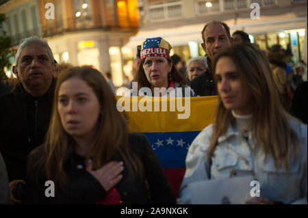 Malaga, Spanien. 16 Nov, 2019. Eine Frau mit einem venezolanischen cap Holding eine Flagge, wie sie singt die Nationalhymne während des Protestes gegen Nicolás Maduro Regierung und zur Unterstützung der Politiker Juan Guaidó, Führer der Opposition und selbst ernannten einstweiligen Präsidenten Venezuelas. Ein demonstrant wird gesehen, die eine venezolanische Flagge während der Protest gegen Nicolás Maduro Regierung und zur Unterstützung der Politiker Juan Guaidó, Führer der Oppositionspartei und selbsternannte interim Präsident von Venezuela. Credit: SOPA Images Limited/Alamy leben Nachrichten Stockfoto