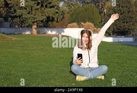 Happy Teenager mit Kopfhörern hört Musik von Ihrem Smartphone in Park Stockfoto