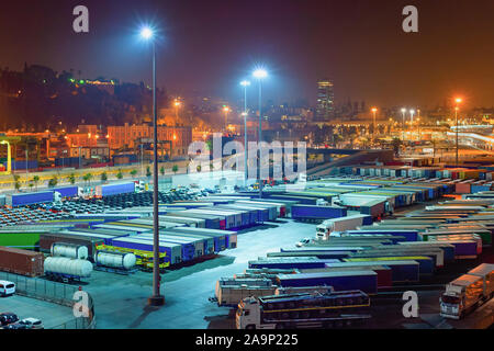 Nachtansicht von Lkw und Cargo Container im Hafen von Barcelona, Straße, Kreuzung, Parkplatz und beleuchtete Skyline im Hintergrund, Spanien Stockfoto