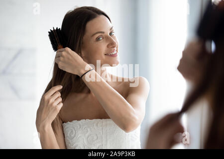 Gerne attraktive junge Frau putzen lange Haare Suchen in Spiegel Stockfoto