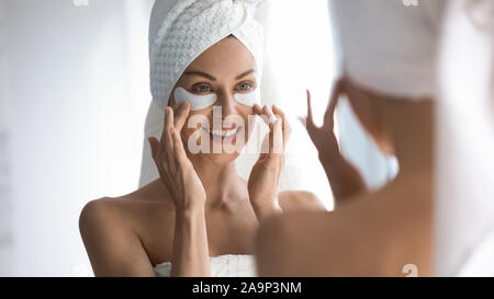 Glückliche Frau Handtuch auf dem Kopf Anwenden von Patches im Spiegel zu betrachten Stockfoto