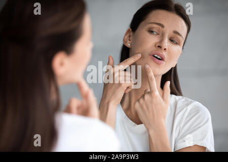 Frustrierte Frau im Spiegel über die Gesichtshaut Problem betont suchen Stockfoto