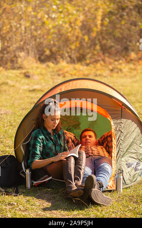 Junge Mädchen ein Buch lesen mit ihrem Freund neben dem Zelt. Entspannen Urlaub Stockfoto