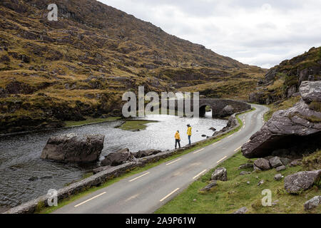 Mutter und Sohn gehen durch den Fluss Loe, schmale Straße durch die Lücke der Dunloe Tal in der macgillycuddy Reeks Berge, Irland, County Kerry. Stockfoto