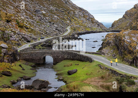 Mutter und Sohn gehen durch den Fluss Loe, schmale Straße durch die Lücke der Dunloe Tal in der macgillycuddy Reeks Berge, Irland, County Kerry. Stockfoto