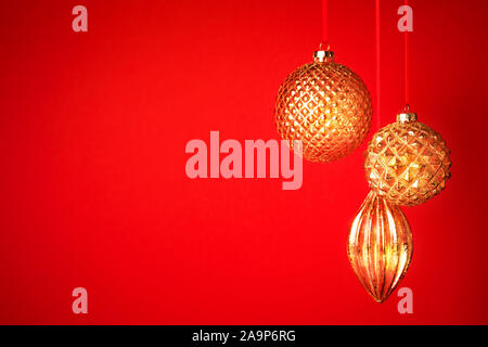 Drei goldene Weihnachtskugeln hängenden gegen den roten Hintergrund. Neues Jahr Grußkarte. Selektive konzentrieren. Stockfoto