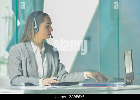 Junge Frau im Büro die Eingabe über Tastatur und sprechen über Kopfhörer Stockfoto