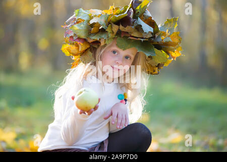 Mädchen im Herbst Park mit einem Kranz von gelben Blätter mit einem Apple. Ein Kind auf einem Spaziergang im Herbst Stockfoto