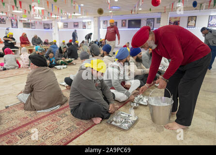 Ein Sikh Mann serviert Speisen in die sitzende Personen n a Langar, eine kostenlose Gemeinschaftsküche. In South Richmond Hill, Queens, New York City. Stockfoto