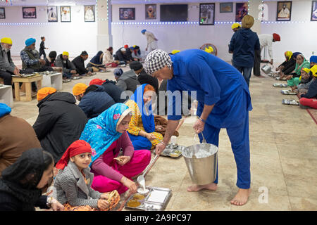 Ein Sikh Mann serviert Speisen in die sitzende Personen n a Langar, eine kostenlose Gemeinschaftsküche. In South Richmond Hill, Queens, New York City. Stockfoto