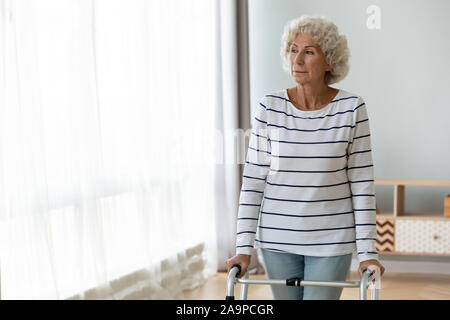 Nachdenkliche traurige verletzt alte Frau alleine stehen mit Gehhilfe Stockfoto