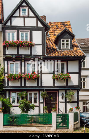 Blick auf einem traditionellen alten Deutschen Haus mit Fachwerk, Fenster dekoriert mit roten Blüten und einem grünen Holz- Absperrung, Quedlinburg. Stockfoto