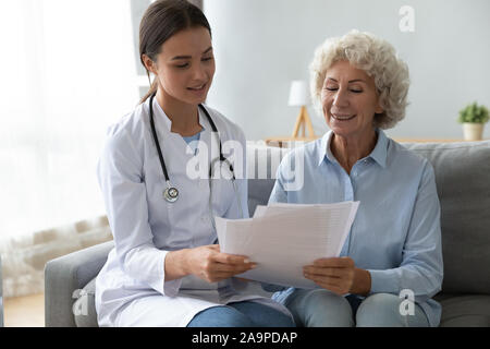 Lächelnde ältere Frau Patienten und jungen Arzt lesen Versicherungsvertrag Stockfoto