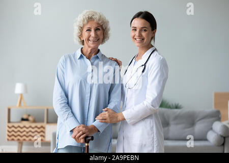Weibliche Krankenschwester helfen, alte Frau mit Stock bei Camera suchen Stockfoto