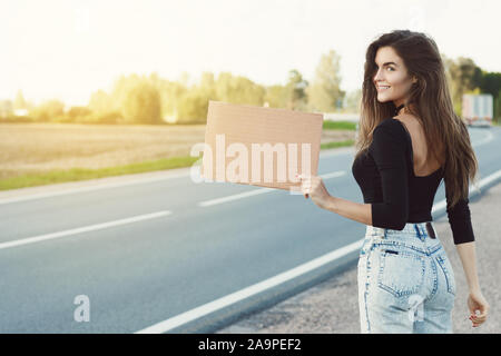 Junge Frau per Anhalter auf der Straße ist mit einem leeren Karton Zeichen Stockfoto