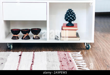 Gemütliche Einrichtung, brennen Spa aroma Kerzen in Kokosnussschalen, Stapel Bücher, auf weißem Glas Nachttisch in der Nähe von einem bunten Teppich Hintergrund Stockfoto