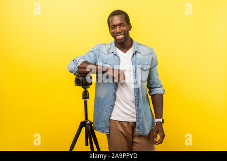Portrait von fröhlichen Fotograf oder Reisenden in Jeans casual Shirt lächelnd und an der Kamera posieren mit professionellen digitalen DSLR-Kamera auf Stativ. indo Stockfoto