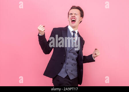 Ja Sieg! Portrait von Crazy enthusiastisch extrem glücklich Geschäftsmann im Tuxedo stehend mit erhobenen Armen und geschlossenen Augen, schreien vor Freude Erfolg Stockfoto