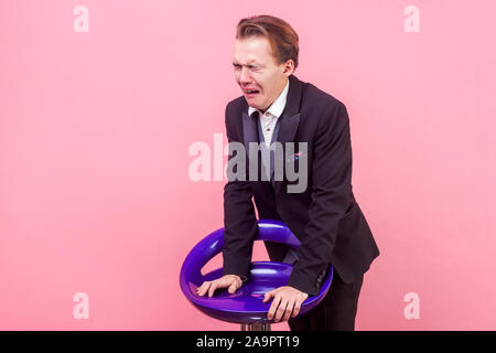 Portrait von dramatischen verzweifelten Mann in Anzug lehnte sich auf Stuhl weinen und schreien mit Grimasse des Schmerzes und geschlossenen Augen tief beleidigt offende Stockfoto