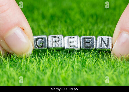 Nahaufnahme auf Wort "Grün" in Metall Buchstaben auf Gras gelegt geschrieben und zwischen die Finger einer Frau. Konzept der Ökologie Hintergrund Stockfoto