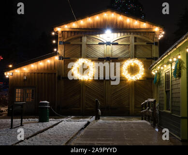 Barn House mit Weihnachtsbeleuchtung dekoriert in einer winternacht fotografiert, dieser Kranz hebt sich der verwitterte Holz- Hintergrund. Stockfoto