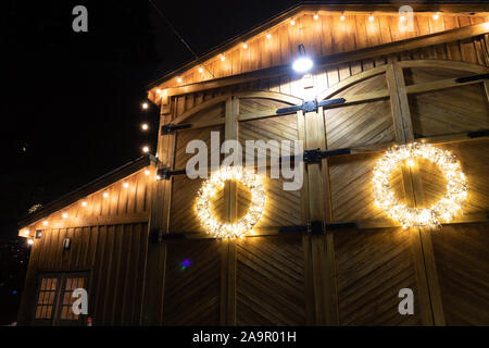 Barn House mit Weihnachtsbeleuchtung dekoriert in einer winternacht fotografiert, dieser Kranz hebt sich der verwitterte Holz- Hintergrund. Stockfoto