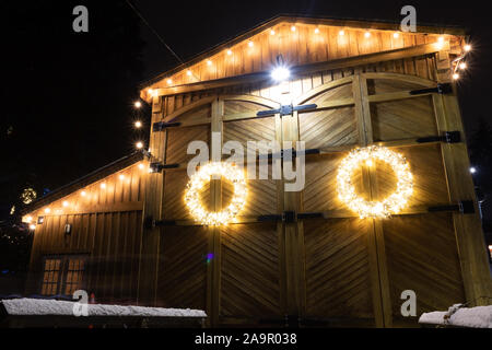 Barn House mit Weihnachtsbeleuchtung dekoriert in einer winternacht fotografiert, dieser Kranz hebt sich der verwitterte Holz- Hintergrund. Stockfoto