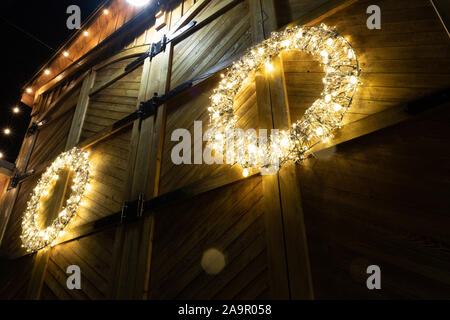 Barn House mit Weihnachtsbeleuchtung dekoriert in einer winternacht fotografiert, dieser Kranz hebt sich der verwitterte Holz- Hintergrund. Stockfoto