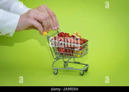 Mini Einkaufswagen voller präsentiert auf grünem Hintergrund. Christmas shopping Konzept Stockfoto