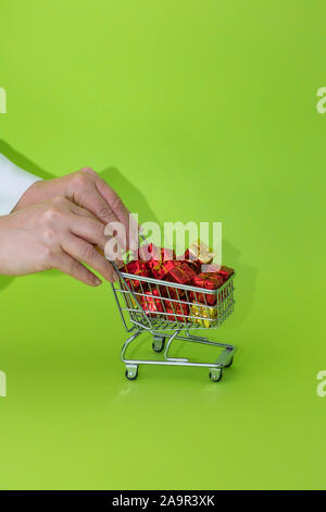 Mini Einkaufswagen voller präsentiert auf grünem Hintergrund. Christmas shopping Konzept Stockfoto