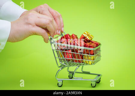Mini Einkaufswagen voller präsentiert auf grünem Hintergrund. Christmas shopping Konzept Stockfoto