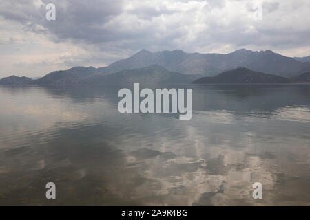 Bewölkter Himmel und ein Nebel über einem See. Albanischen Berge im Hintergrund. Zum Skutarisee, Montenegro. Stockfoto