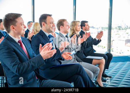 Gruppe von Geschäftsleuten in formale sitzen auf den Stühlen im Konferenzsaal und applaudieren zu Lautsprecher Stockfoto