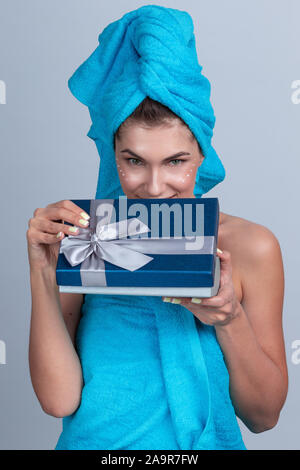 Schöne Frau mit Handtuch auf dem Kopf Creme zur Anwendung nach der Dusche und offenen Geschenkbox Stockfoto